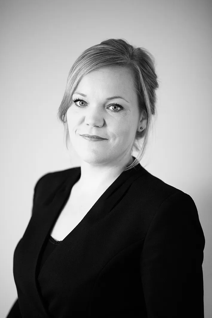 Black and white headshot of a woman with blonde hair in a black blazer with a confident smile