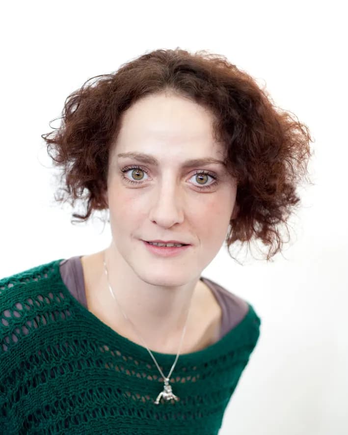 Professional headshot of a person with styled hair in business attire on a neutral background