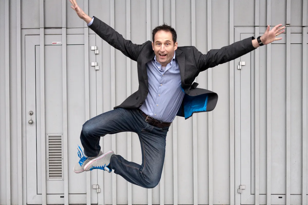 Energetic business portrait of a man in a blazer jumping with arms spread against a metal wall