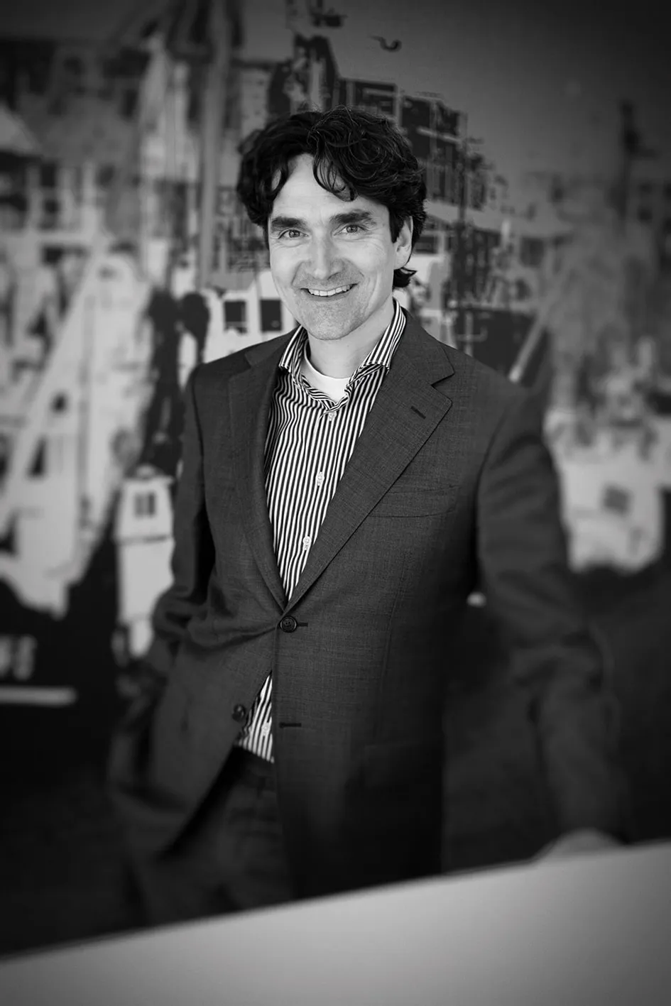 Black and white business portrait of a man in a suit by tall windows with natural side light