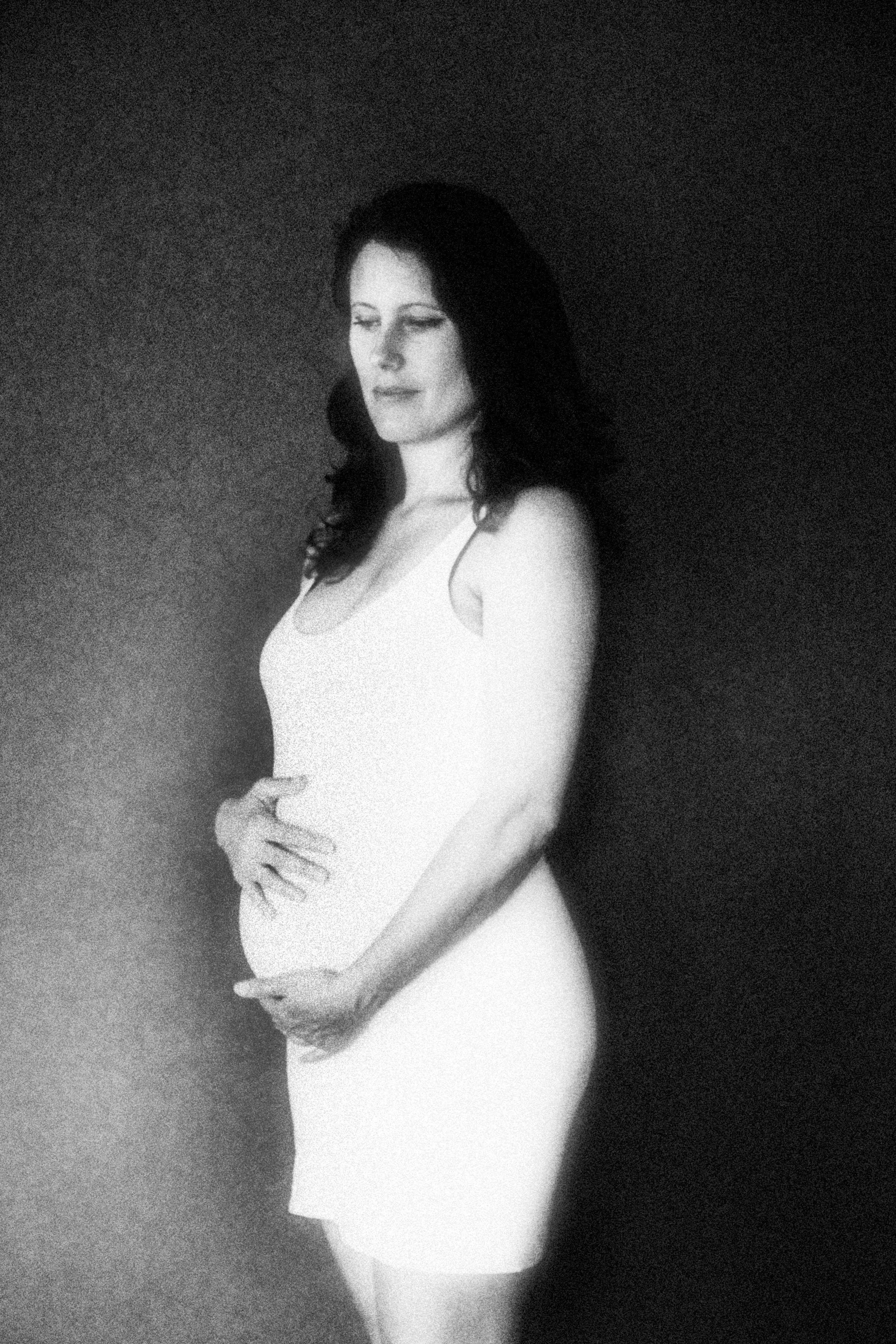 Intimate maternity portrait of a pregnant woman in profile surrounded by soft natural light