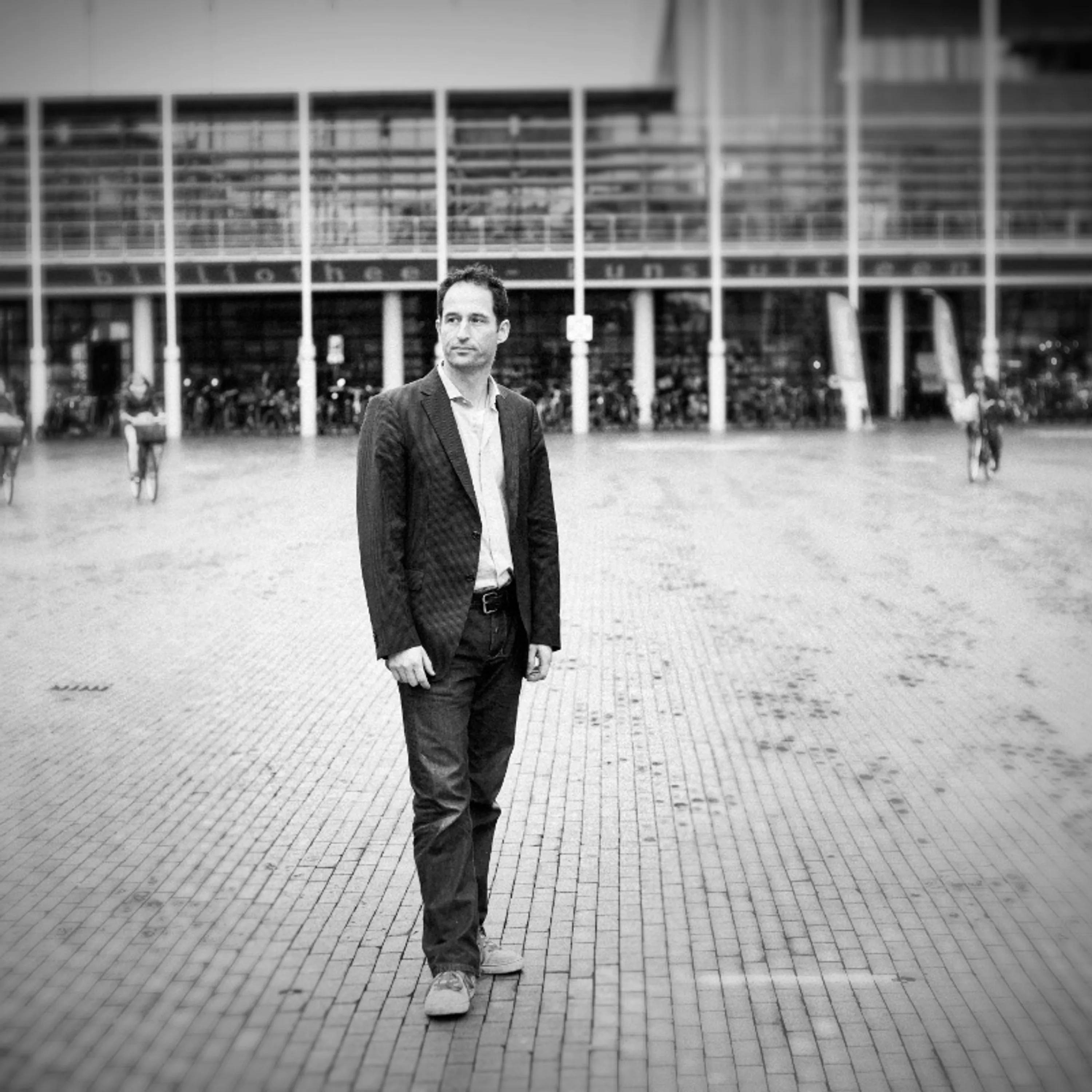 Business portrait of a man in a dark suit standing by large windows in a bright corporate lobby