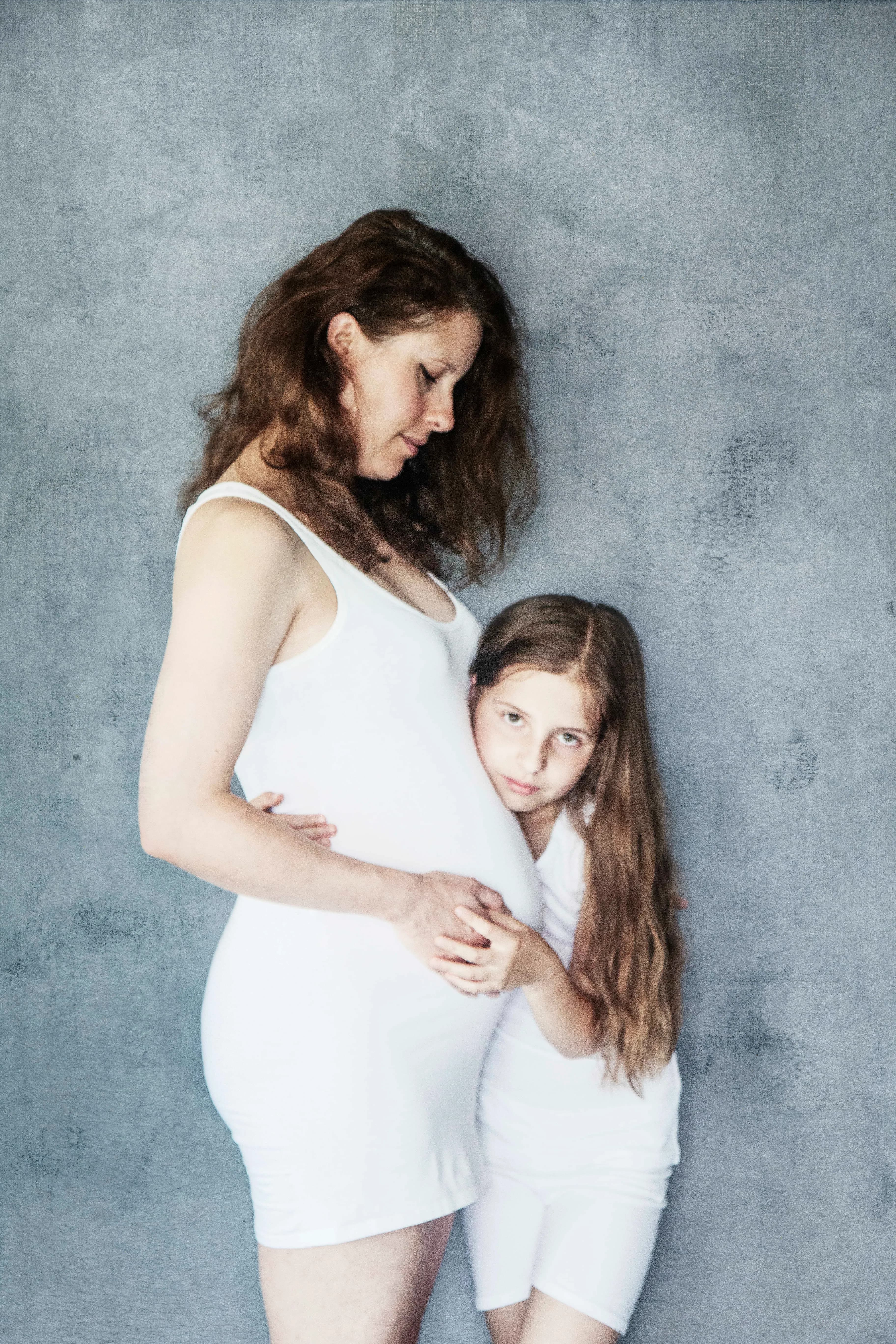 Dreamy maternity portrait of a pregnant woman in white surrounded by blue ethereal clouds