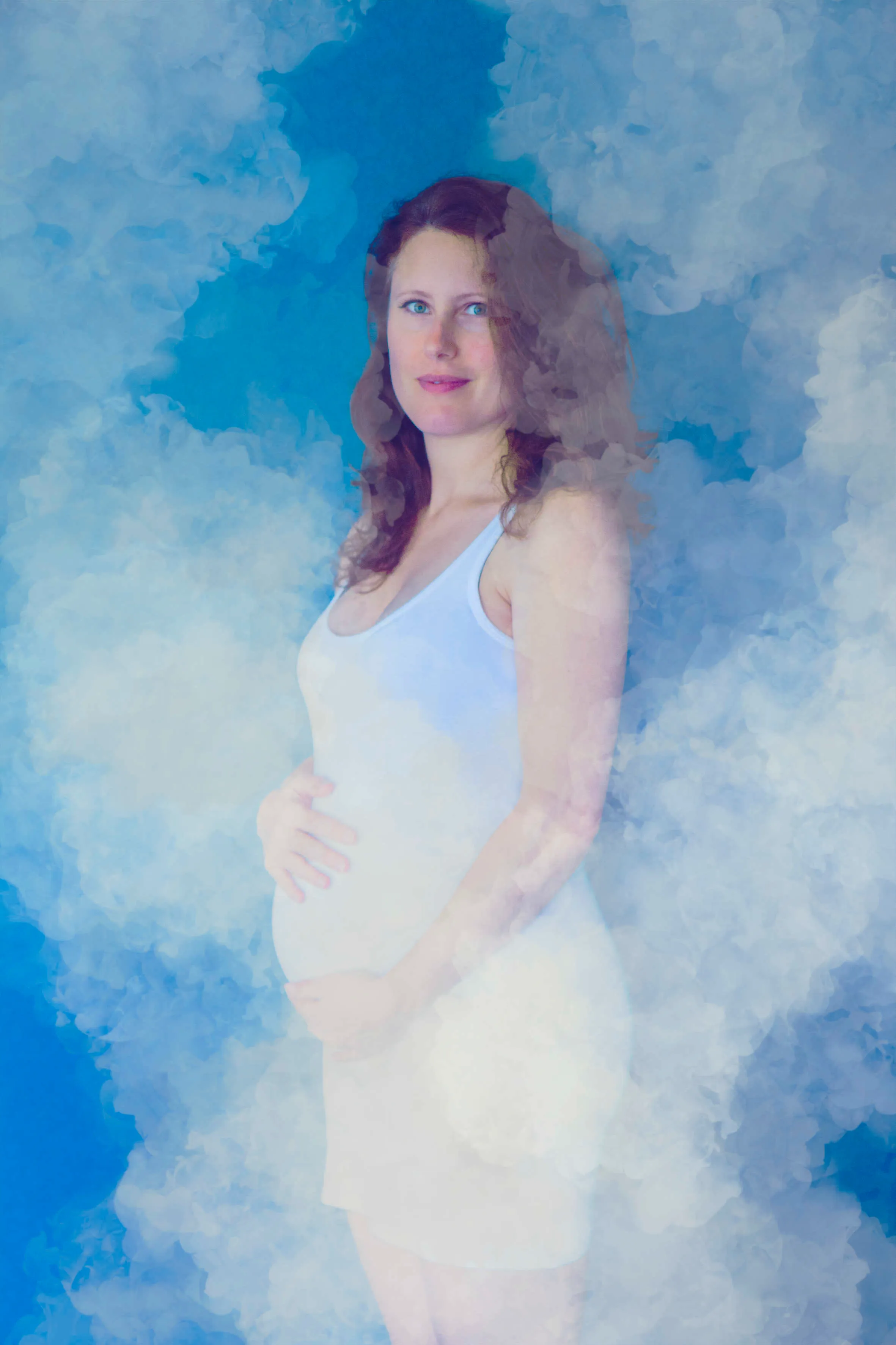 Ethereal maternity portrait of a pregnant woman in white amid soft blue clouds with a serene look