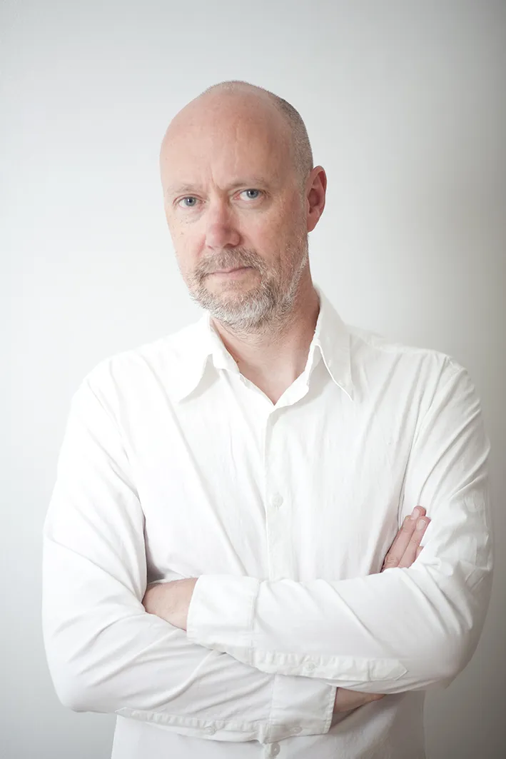 Professional headshot of a man with a beard in a white shirt with arms crossed looking confident